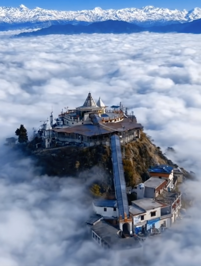 Chandrabadni Temple atop a mountain peak above the clouds, with snow-capped Himalayas in the background